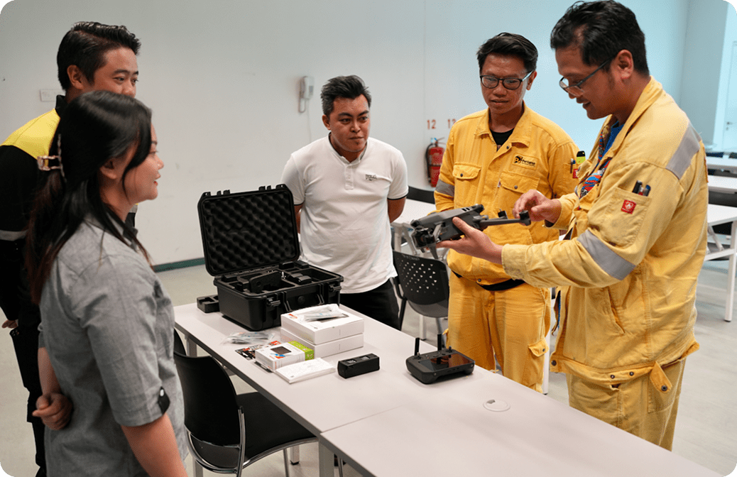 Group of workers receiving hands-on drone training indoors, with equipment and accessories displayed on a table.
