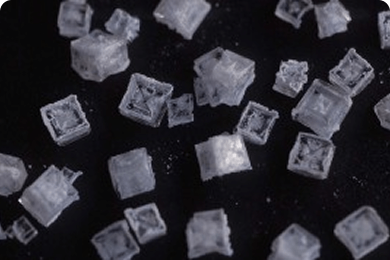 Close-up of salt crystals on a dark surface, showing detailed cube-shaped structures.
