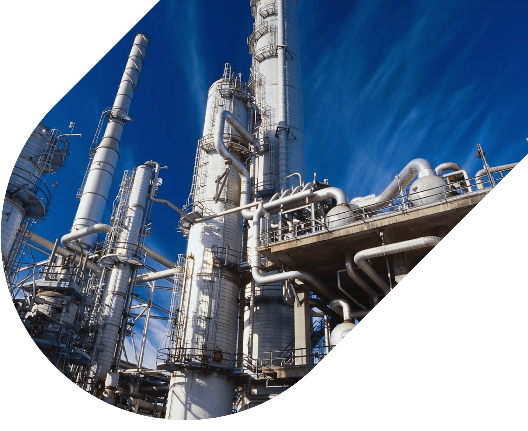 Industrial oil and gas refinery with tall distillation towers, steel pipelines, and structural platforms under a clear blue sky.