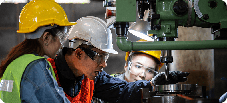 Engineer instructing two trainees on operating a vertical milling machine in an industrial workshop.