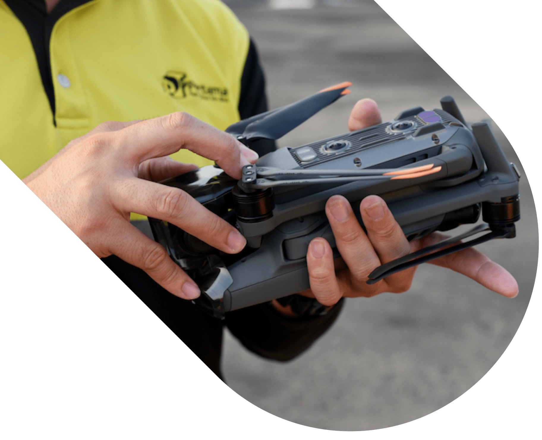 Person holding and adjusting a folded black drone with orange-tipped propellers, wearing a yellow and black uniform.