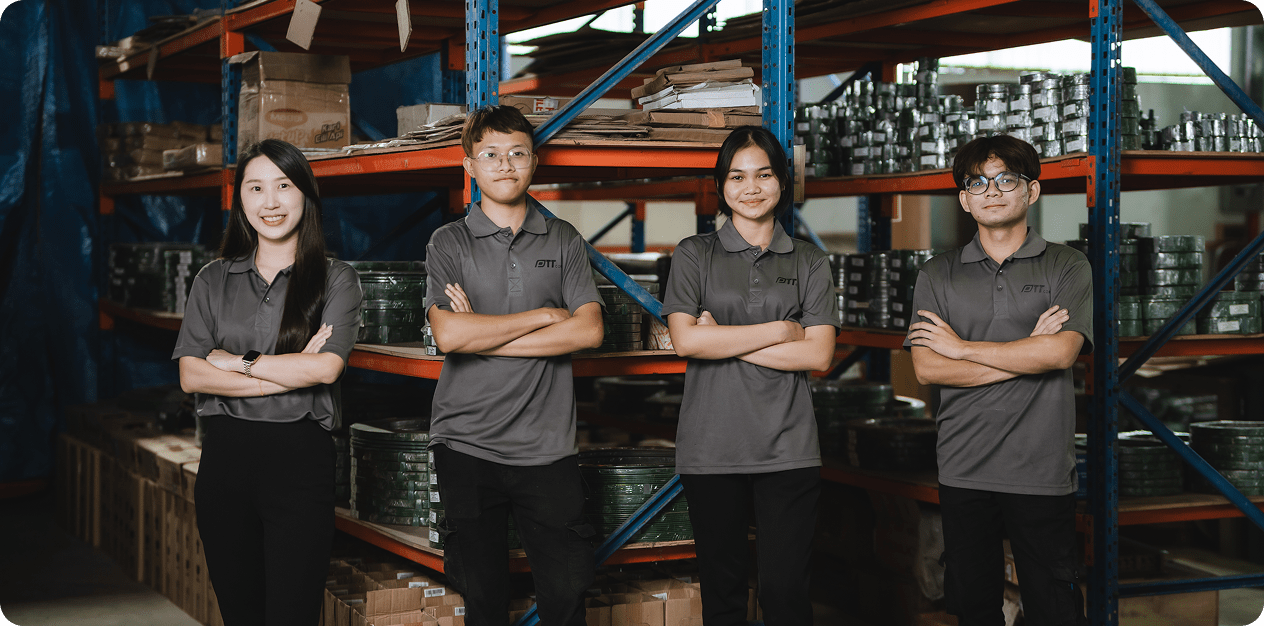 Four warehouse staff in gray uniforms posing confidently in front of industrial shelves.
