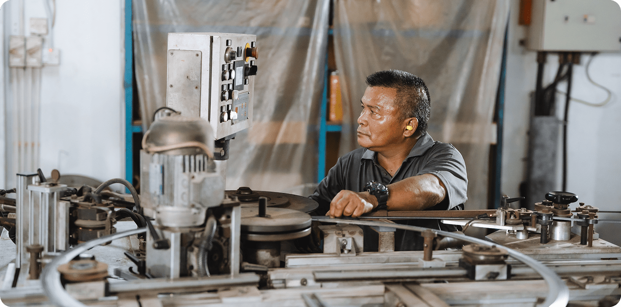 Factory worker operating industrial bending machine with control panel in a manufacturing setting.