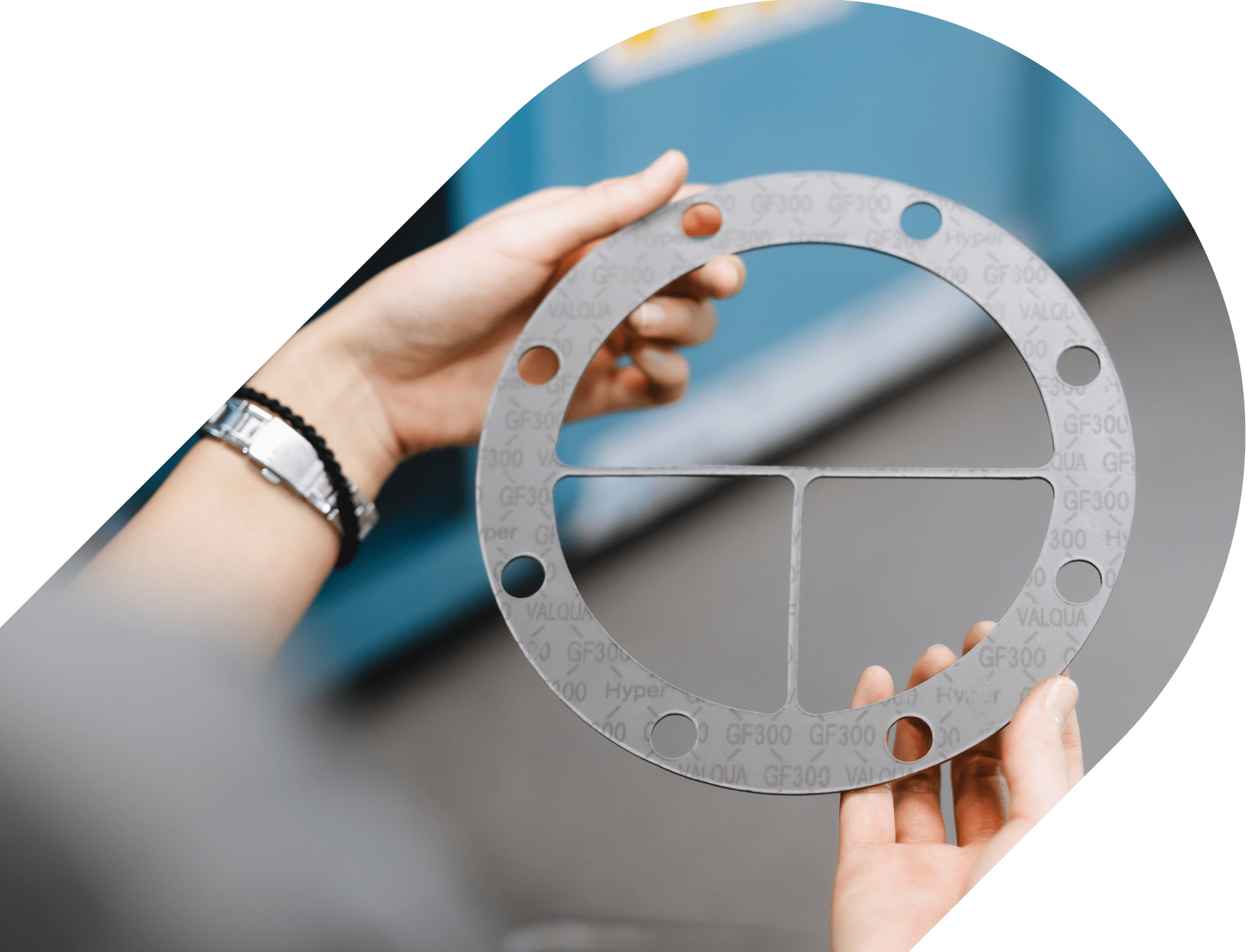 Person holding a circular industrial flange gasket marked "GF300 VALQUA," used for sealing pipe joints.