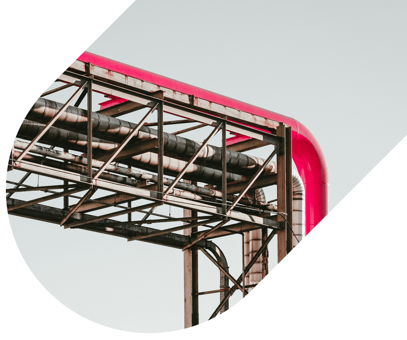 Industrial pipeline system with exposed metal pipes and a prominent red overhead pipe supported by a steel framework against a clear sky.