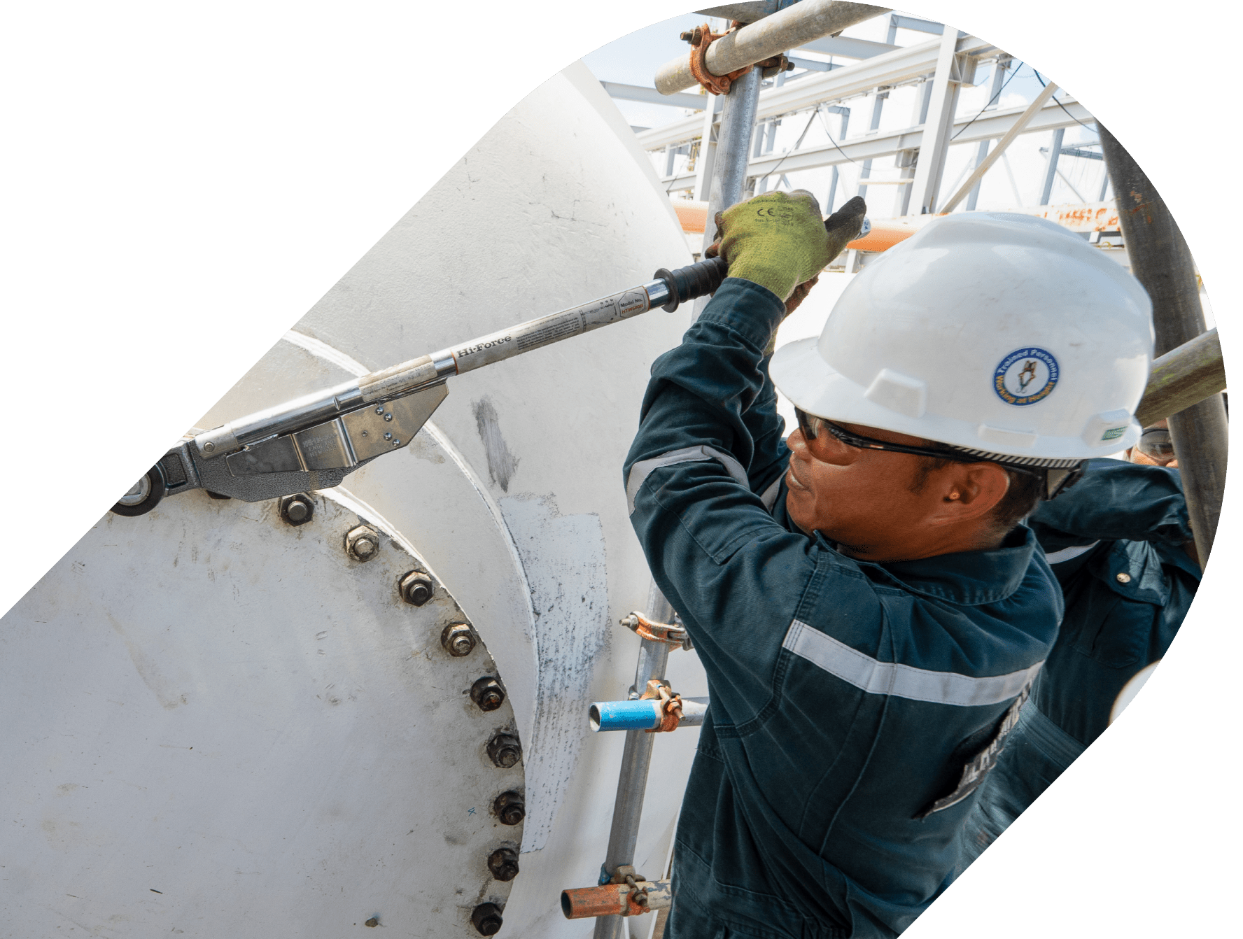 Technician in safety gear using a torque wrench to tighten bolts on a large industrial flange connection.