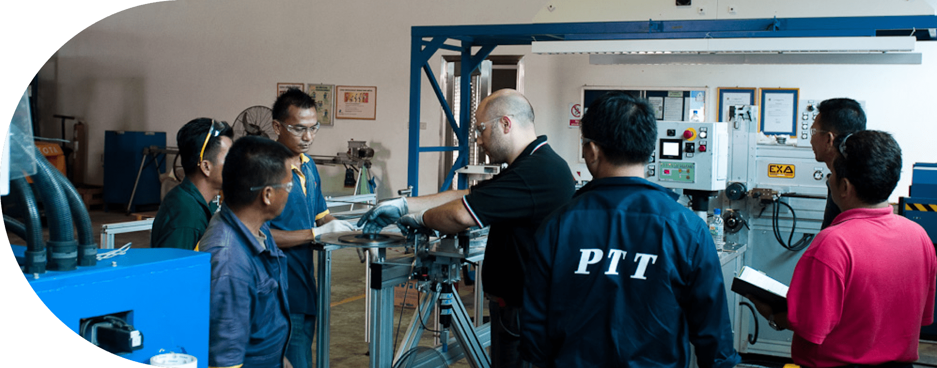 Group of factory workers receiving hands-on machine operation training around industrial equipment in a manufacturing facility.